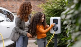  Een vrouw en haar dochter laden hun auto op bij een oplaadstation voor elektrische voertuigen.