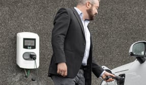 Een man in pak met een accupomp in de hand. Hij laadt zijn auto op.