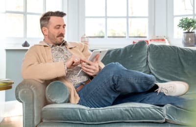 Un homme est assis sur un canapé et utilise sa tablette. 