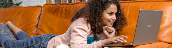 Een vrouw ligt op haar bank achter haar computer