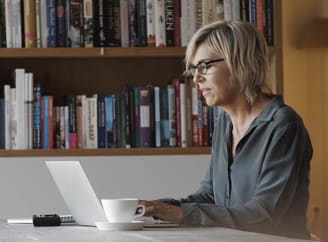 Een vrouw met een bril zit aan een tafel met een laptop voor zich.