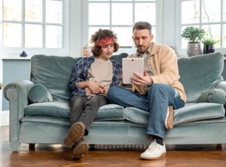 Een vader en zoon op een bank kijken naar een iPad 