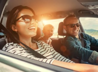 Een gezin (een man aan de bestuurderskant, een vrouw aan de passagierskant en een klein jongetje dat achter zijn vader zit) in een auto genietend van een zonnige dag.