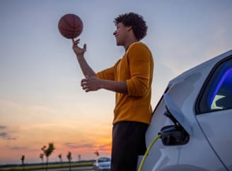 Un jeune garçon est posé sur sa voiture et fait tourner une balle de basket sur son doigt pendant que sa voiture se charge.
