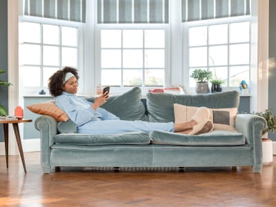 Een vrouw ligt comfortabel in een zetel en glimlacht naar de smartphone in haar hand, tevreden met het onderhoudscontract.