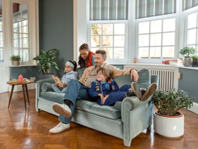 Een vader met drie kinderen zitten samen comfortabel in de zetel, genietend van een goed werkende verwarmingsketel.