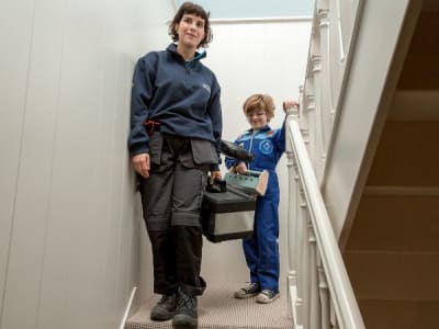 Een technieker van ENGIE en een kind staan met een toolkit op de trap, klaar voor ketelonderhoud.
