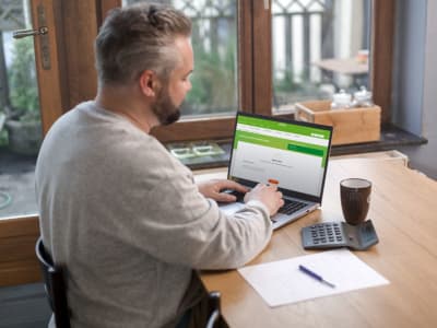 Un homme assis à une table, utilisant un ordinateur portable et une calculatrice pour travailler.