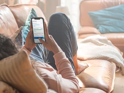 Une femme utilise sa tablette tout en étant assise sur le canapé, concentrée sur son écran.