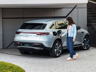 Une femme en train de recharger sa voiture grise à l'extérieur d'un bâtiment