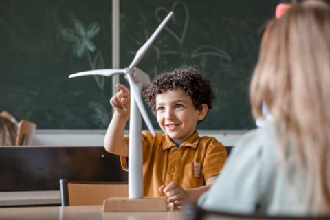 Een jongen en een meisje zitten aan een tafel, met een windturbine op de achtergrond