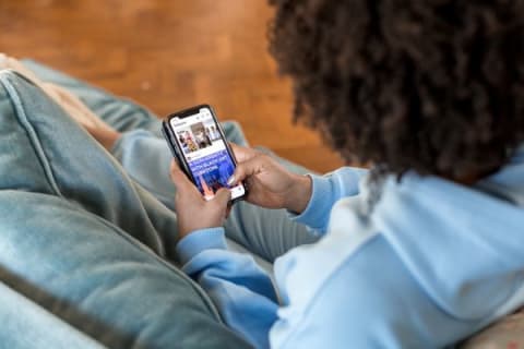 Une femme est assise sur un canapé. Elle regarde son téléphone et est sur les réseaux sociaux.