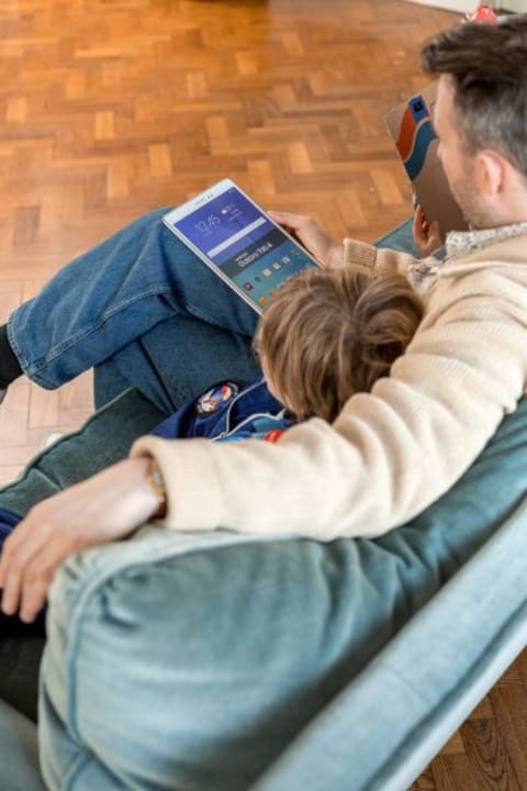 Un homme et un enfant assis sur un canapé tout en regardant la tablette.