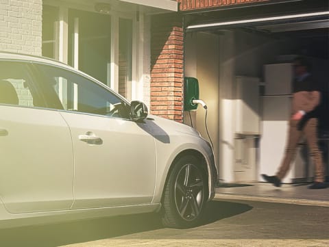 Een man in een garage loopt naar het oplaadpunt voor een witte auto die aan het opladen is.