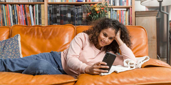 Een vrouw ligt op een bank met haar telefoon in de hand