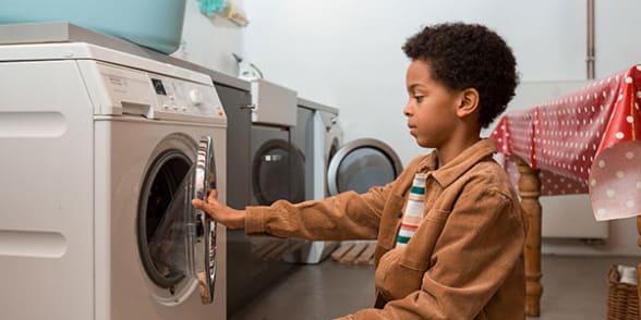 Een jongen staat voor een wasmachine