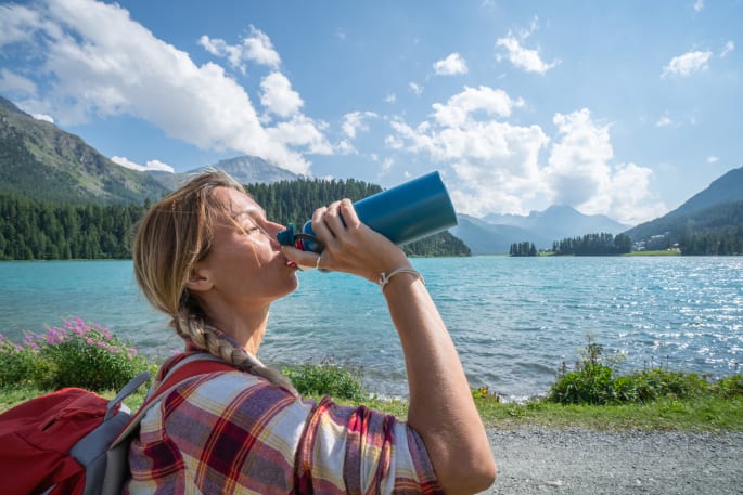 Vrouw in de bergen die van een drinkbus drinkt