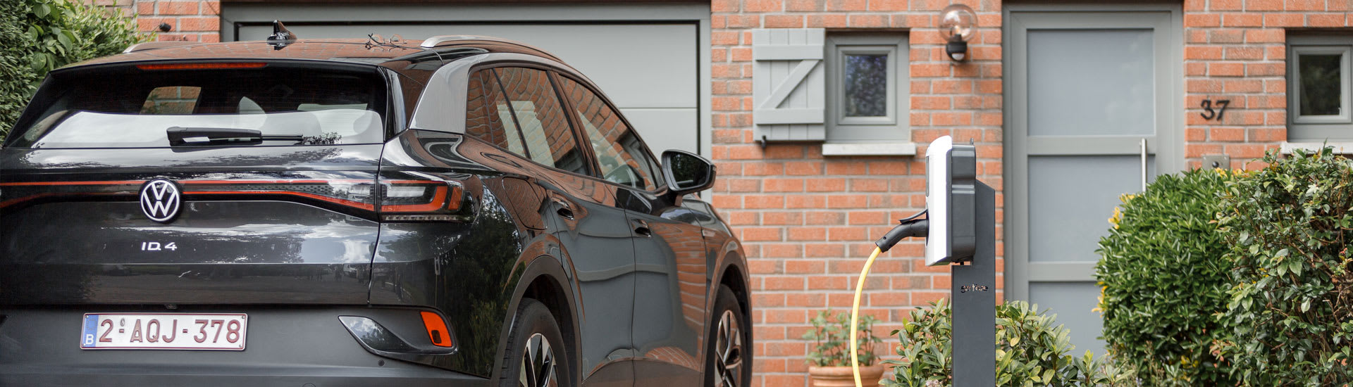 Er staat een zwarte auto geparkeerd voor het huis en hij is aan het opladen aan het thuislaadstation.