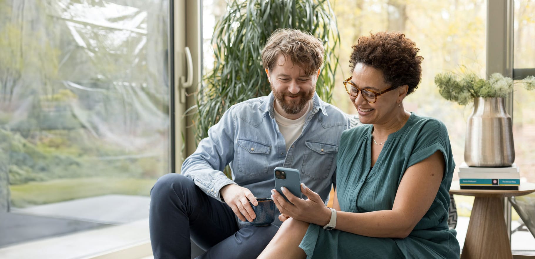 Een man en een vrouw zitten samen en kijken geïnteresseerd naar een mobiele telefoon.