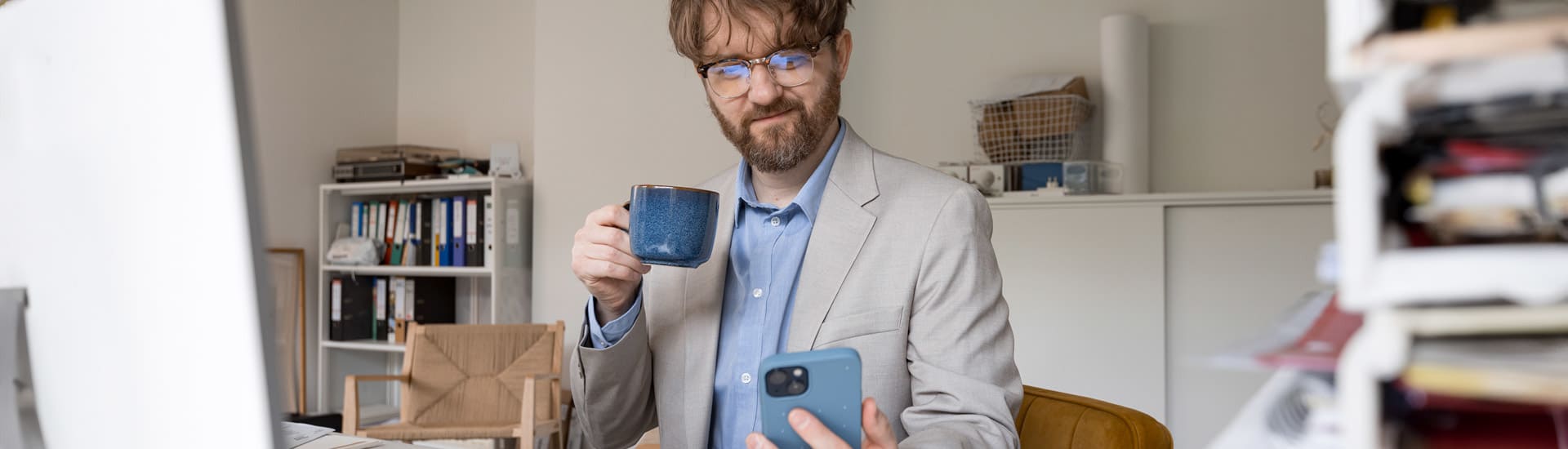 Un homme assis à son bureau, avec son téléphone et une tasse à la main