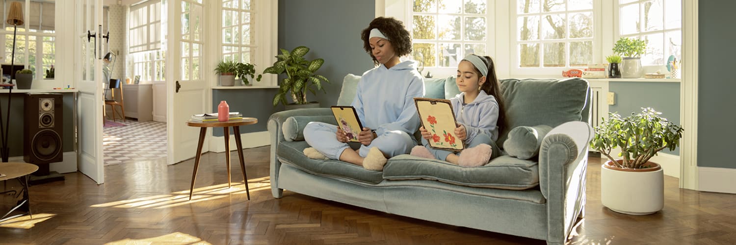 Une femme et une jeune fille sont assises sur un canapé et regardent leur tablette.