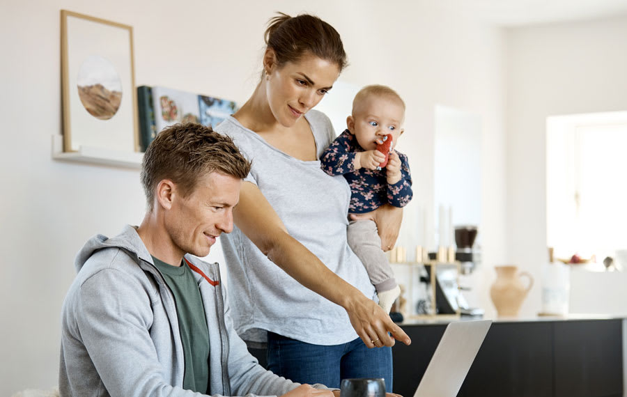 Un homme regarde un écran d&#039;ordinateur et, à côté de lui, une femme tient un bébé et regarde également l&#039;écran en même temps.