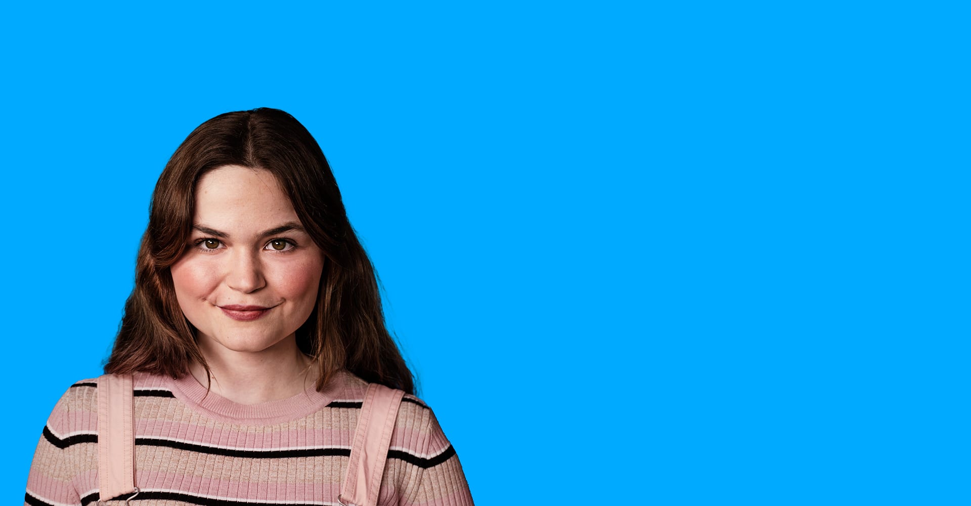 Une femme aux longs cheveux bruns se tient devant un fond bleu.