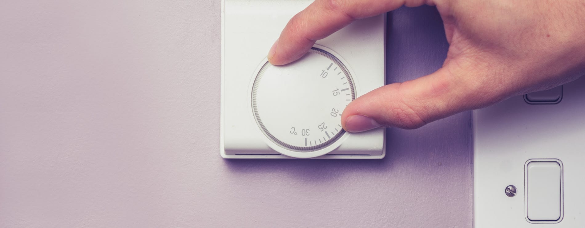 Eén persoon stelt een thermostaat in aan de muur om de kamertemperatuur aan te passen.